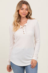woman wearing a cream long sleeve henley top with ruffle detail and button closure paired with blue jeans