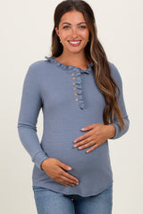 woman wearing a blue maternity top with a ruffle detail and button accents, holding her baby bump