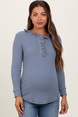 woman wearing a blue ribbed maternity top with ruffle collar and button detail, showing her baby bump