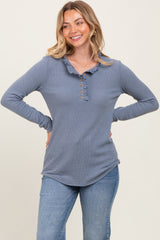 woman wearing a blue long sleeve henley top with a ruffled collar and button details, smiling with hands on hips