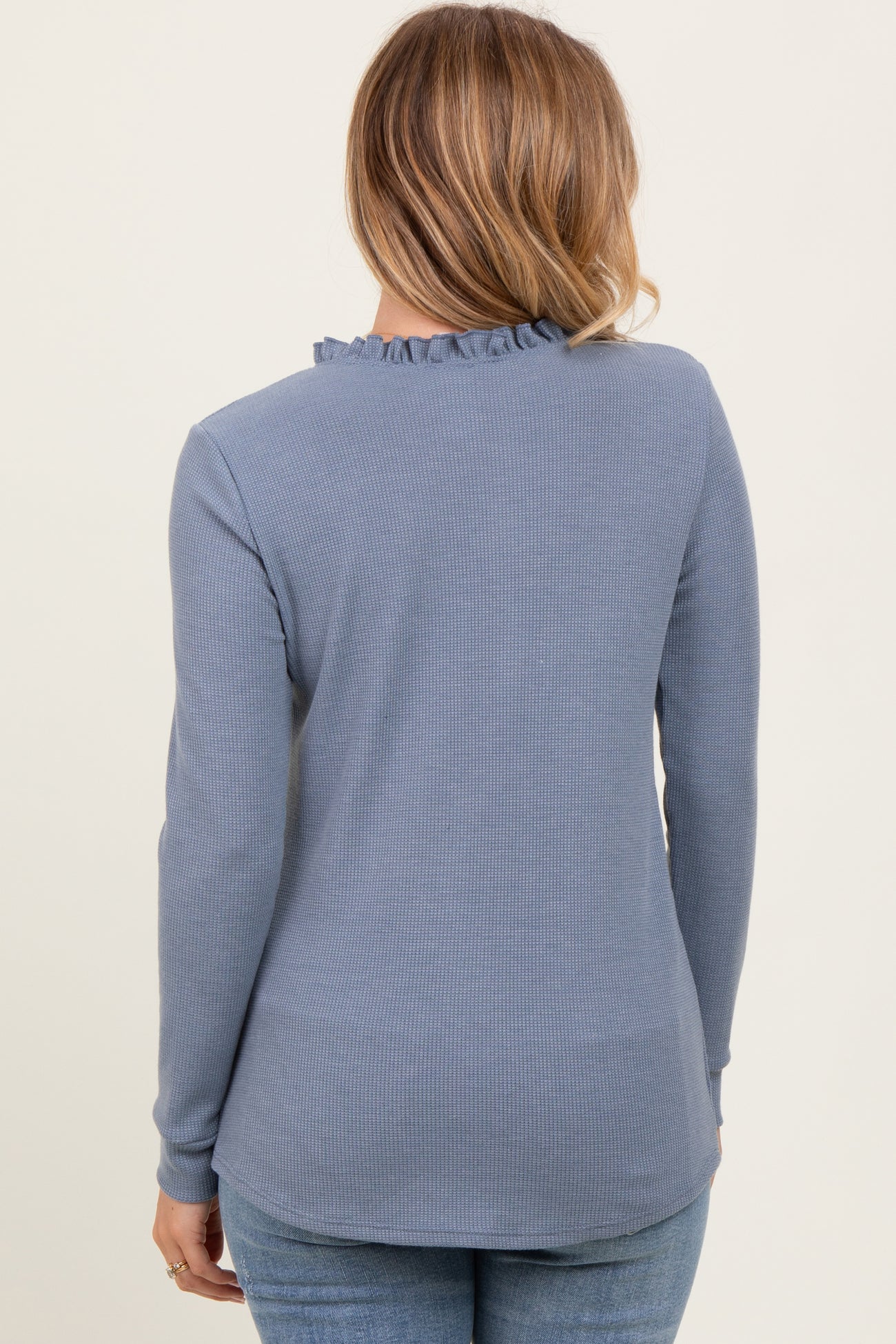 woman wearing a light blue long sleeve top with ruffle neckline and textured fabric, viewed from the back