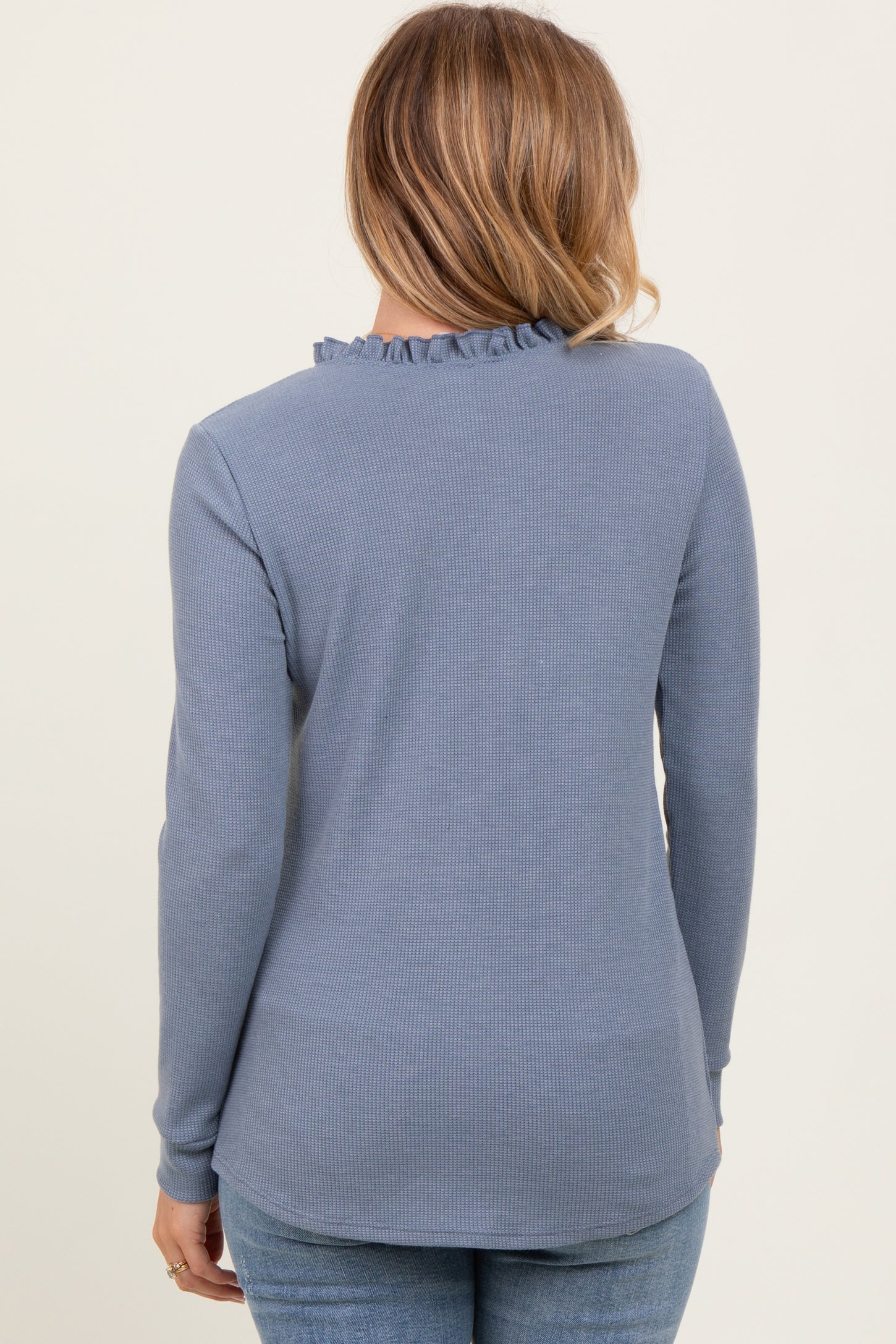 woman wearing a light blue long sleeve top with ruffle neckline and textured fabric, viewed from the back