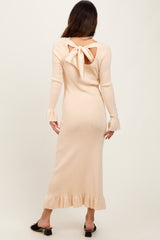 woman wearing a light peach ribbed midi dress with a back cutout and bow detail, featuring ruffled sleeves and hem