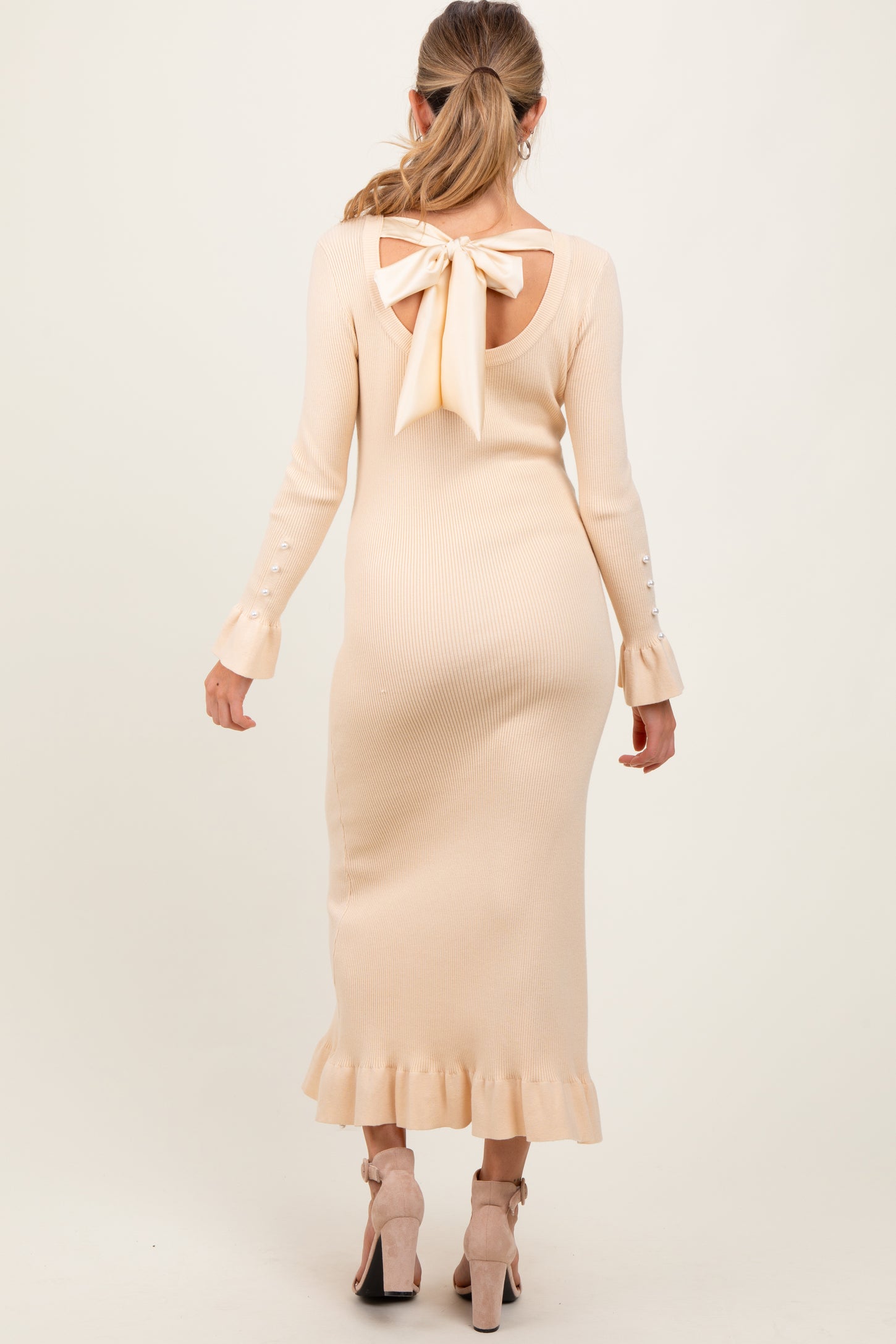 woman wearing a light beige ribbed maternity dress with a bow detail at the back and ruffle hem