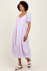woman wearing a lavender striped midi dress with puff sleeves and a tiered hem, standing and smiling