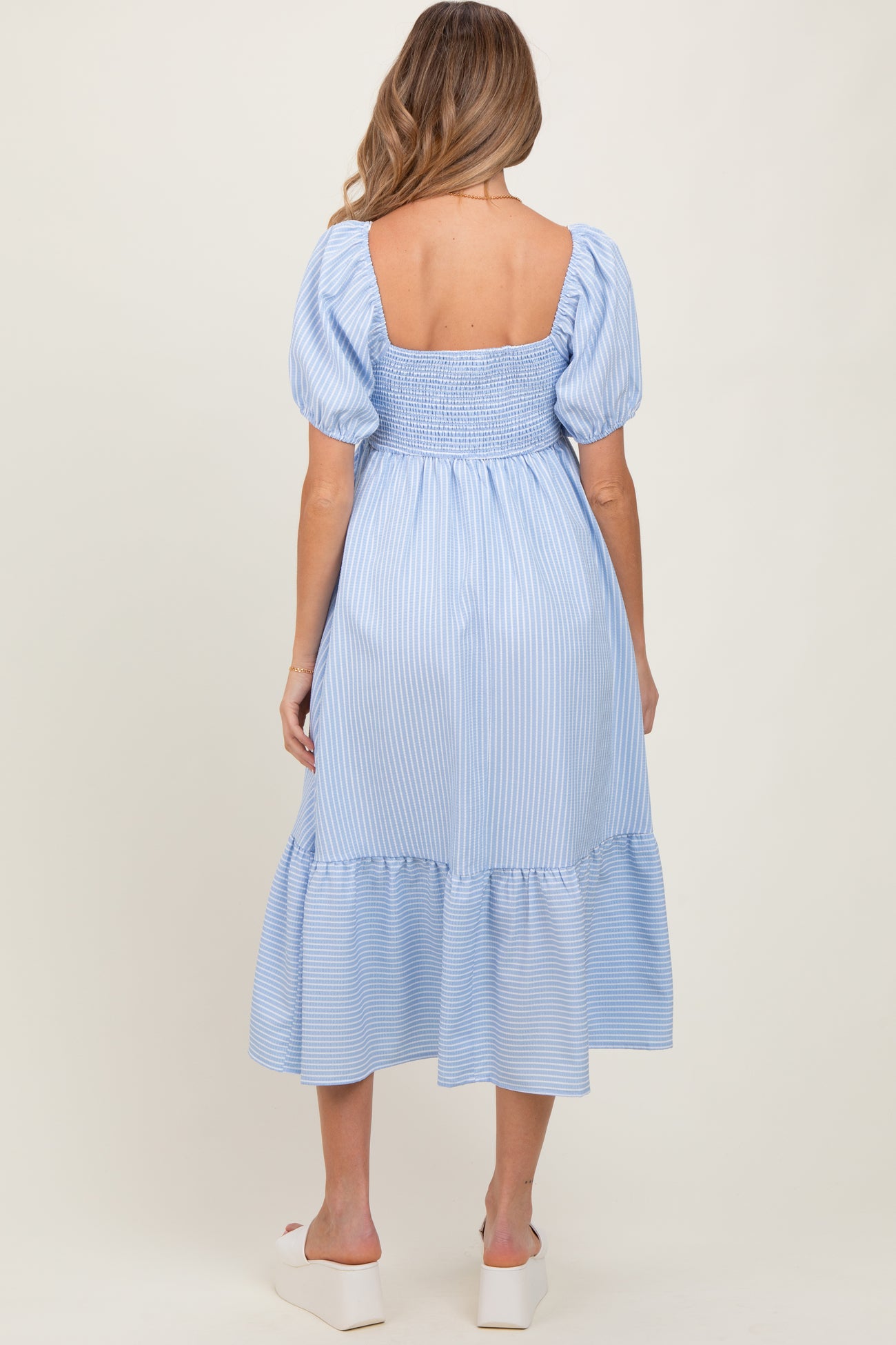 woman wearing a light blue striped maternity dress with puff sleeves and a tiered hem, showing her back