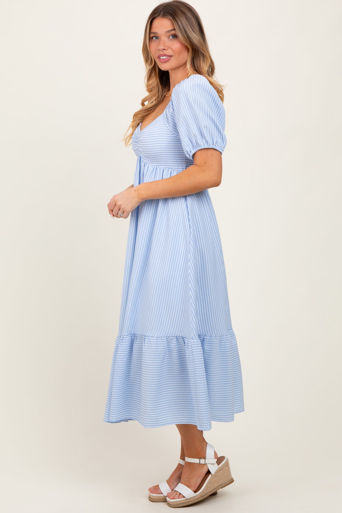 woman wearing a light blue striped puff sleeve midi dress with a tiered skirt and wedge sandals