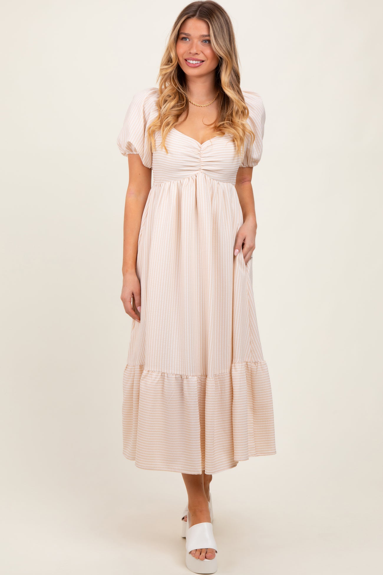 woman wearing a light beige striped puff sleeve maxi dress with a gathered bodice and tiered hem