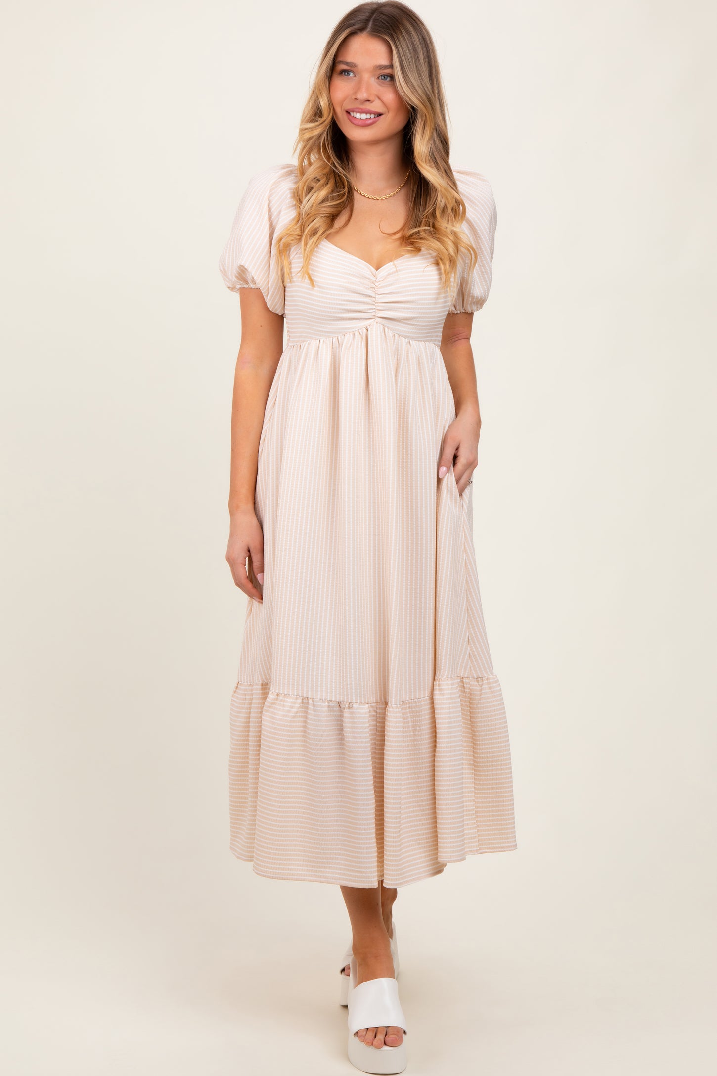woman wearing a light beige striped puff sleeve maxi dress with a gathered bodice and tiered hem