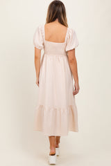 woman wearing a light pink striped maxi dress with puff sleeves and a smocked bodice, standing with her back to the camera