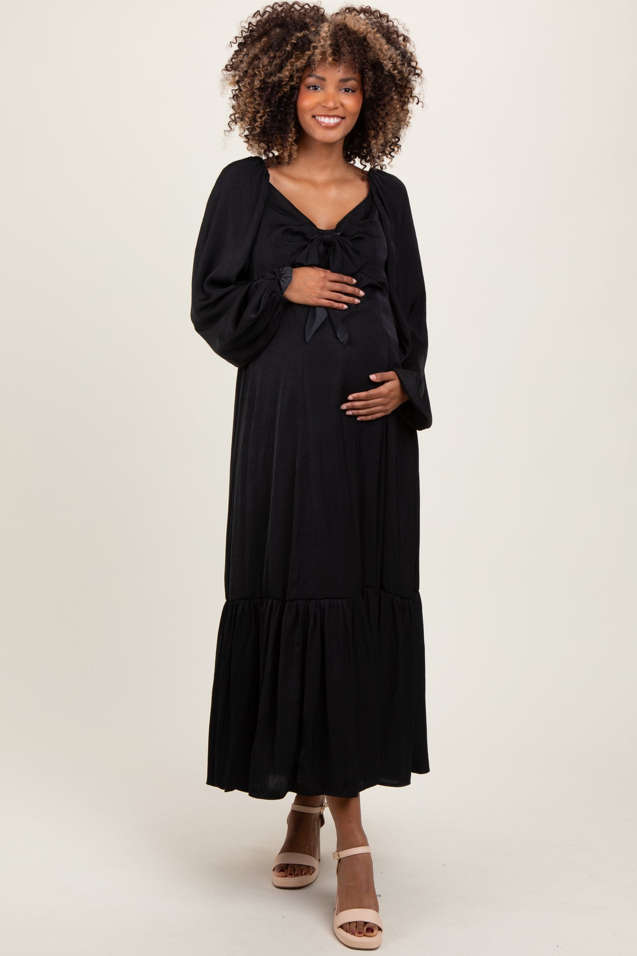 woman wearing a black maternity maxi dress with a bow detail and a ruffled hem, holding her baby bump