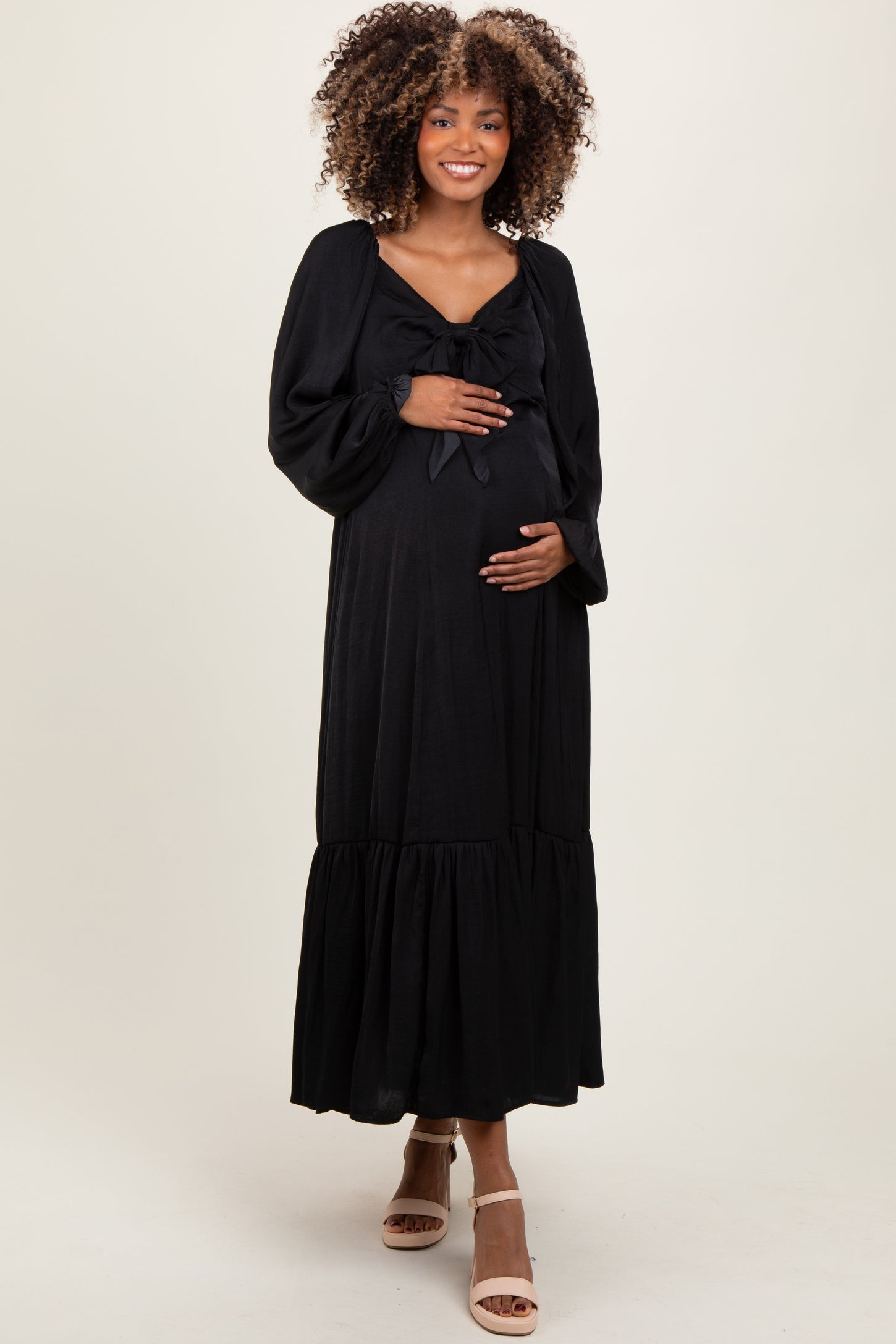 woman wearing a black maternity maxi dress with a bow detail and a ruffled hem, holding her baby bump