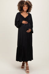 woman wearing a black maternity maxi dress with a bow detail and a ruffled hem, holding her baby bump