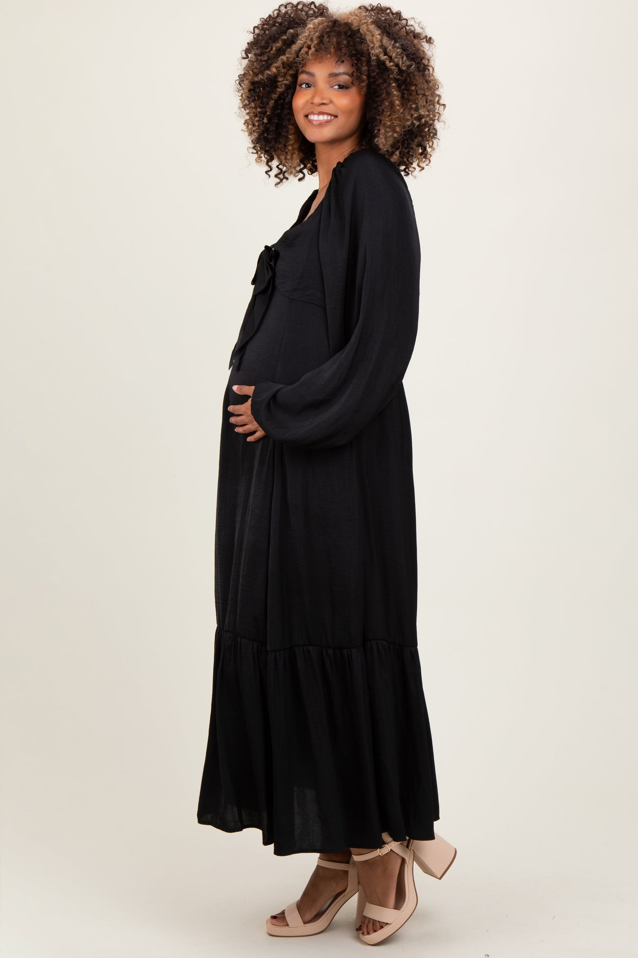 woman wearing a black maternity maxi dress with a bow detail and holding her baby bump