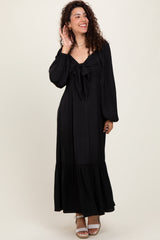 woman wearing a black maxi dress with a tie front and balloon sleeves, standing and smiling