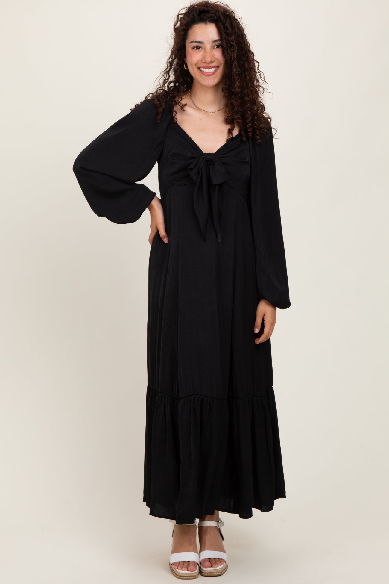 woman wearing a black long sleeve maxi dress with a tied front detail and a tiered hem, smiling at the camera