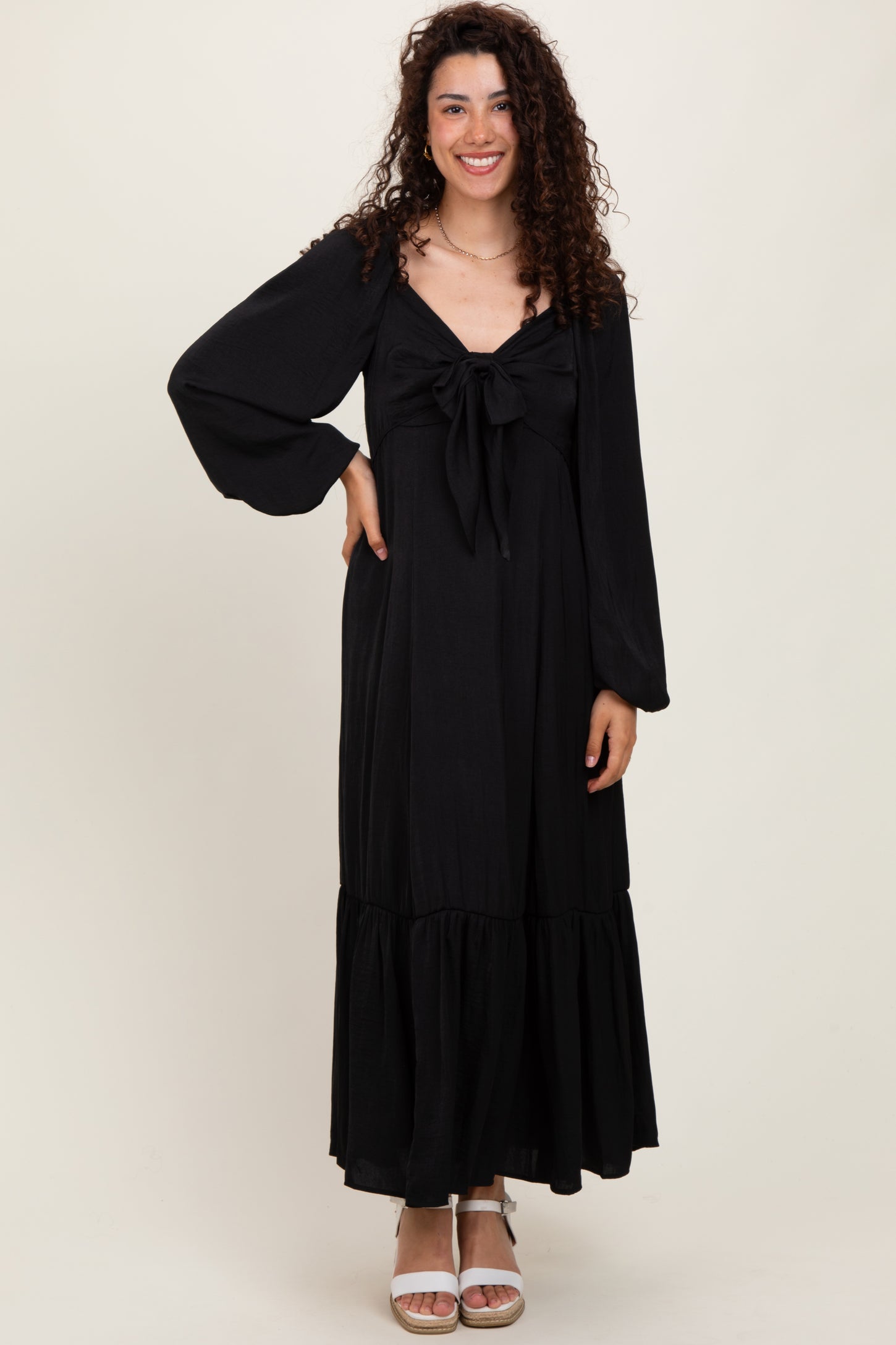 woman wearing a black long sleeve maxi dress with a tied front detail and a tiered hem, smiling at the camera