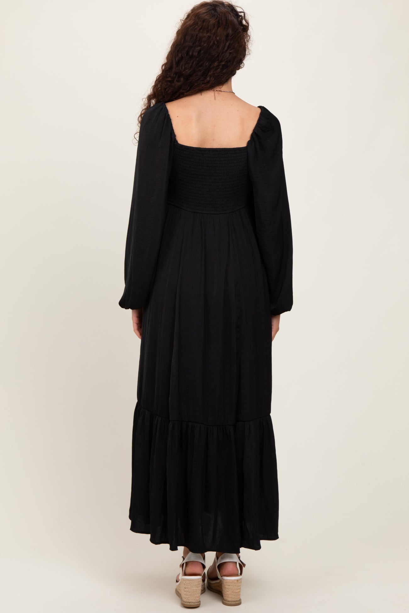 woman wearing a black long sleeve maxi dress with a smocked bodice and tiered skirt, shown from the back