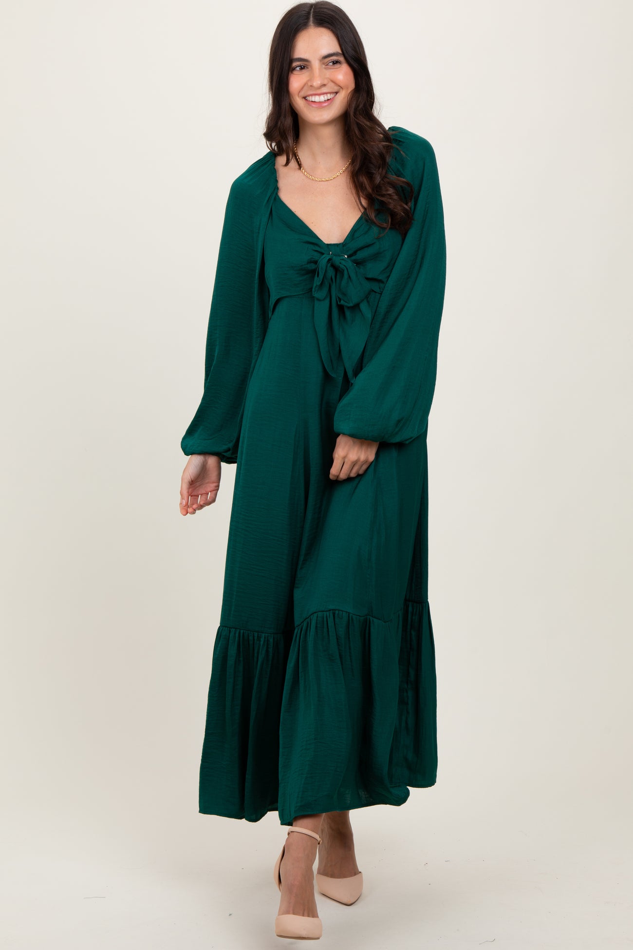woman wearing a green maxi dress with a knotted bodice and puff sleeves, standing with a smile on a neutral background