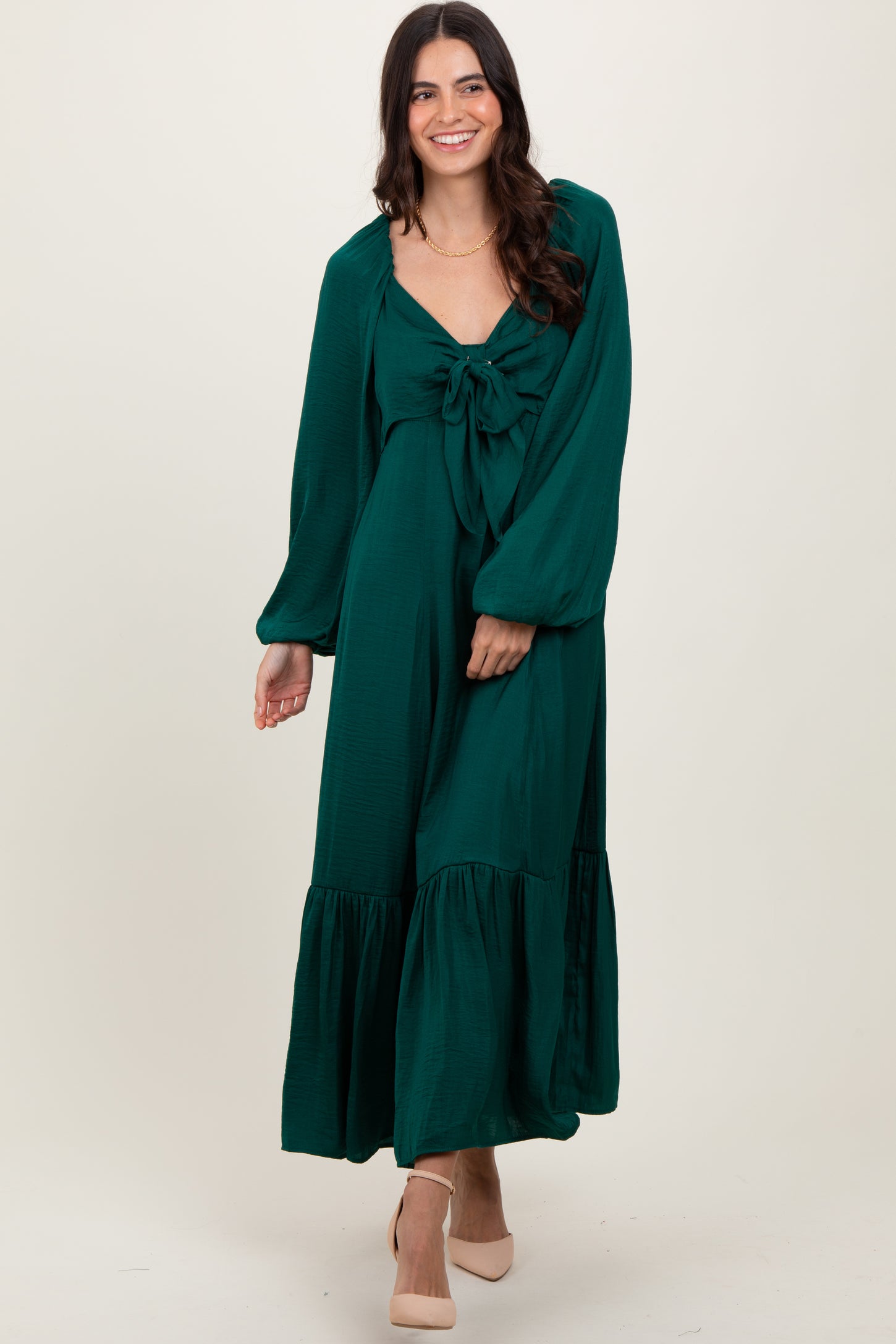 woman wearing a green maxi dress with a knotted bodice and puff sleeves, standing with a smile on a neutral background