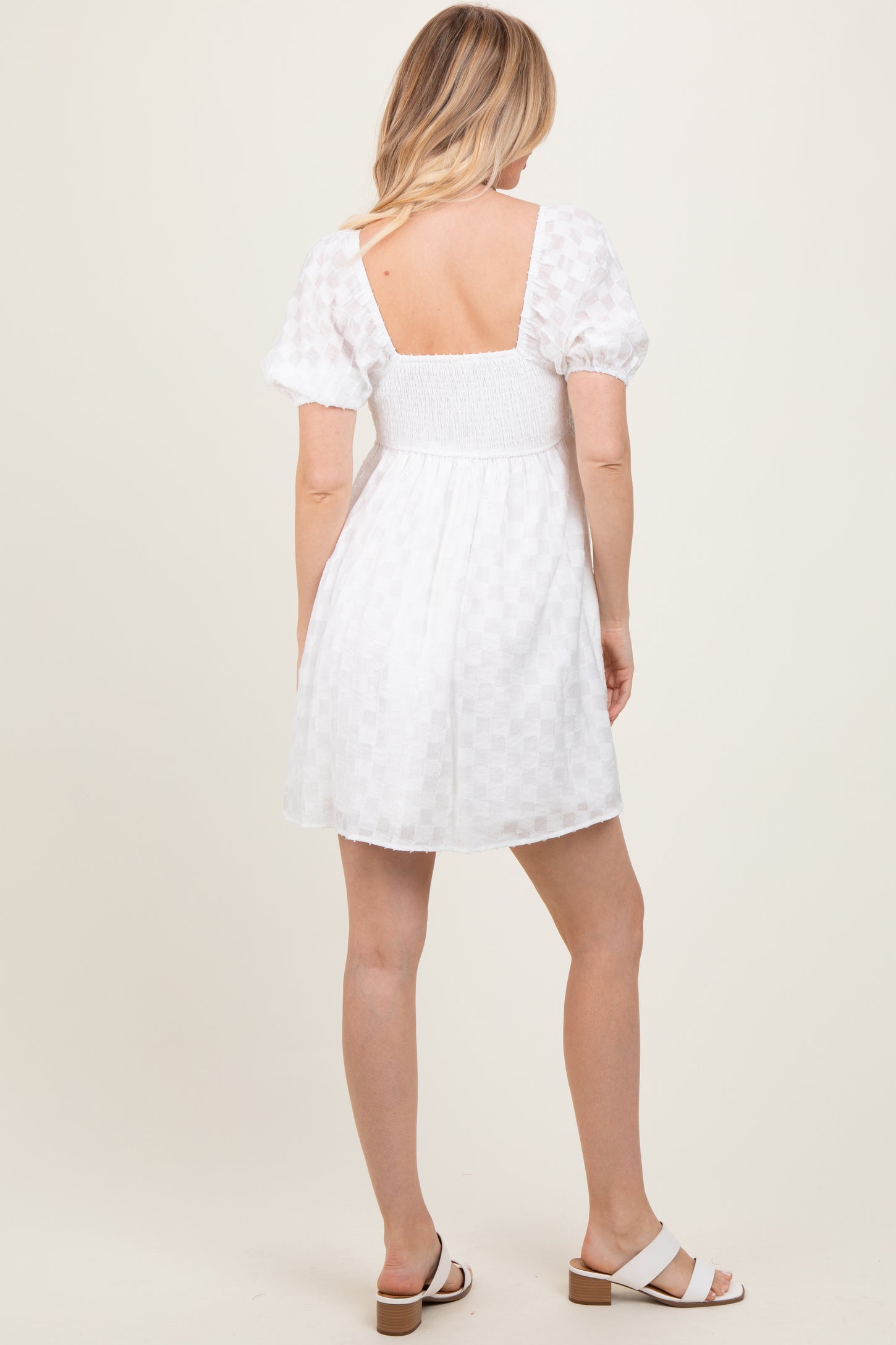 woman wearing a white short puff sleeve dress with a smocked back and checkered texture, standing with her back to the camera
