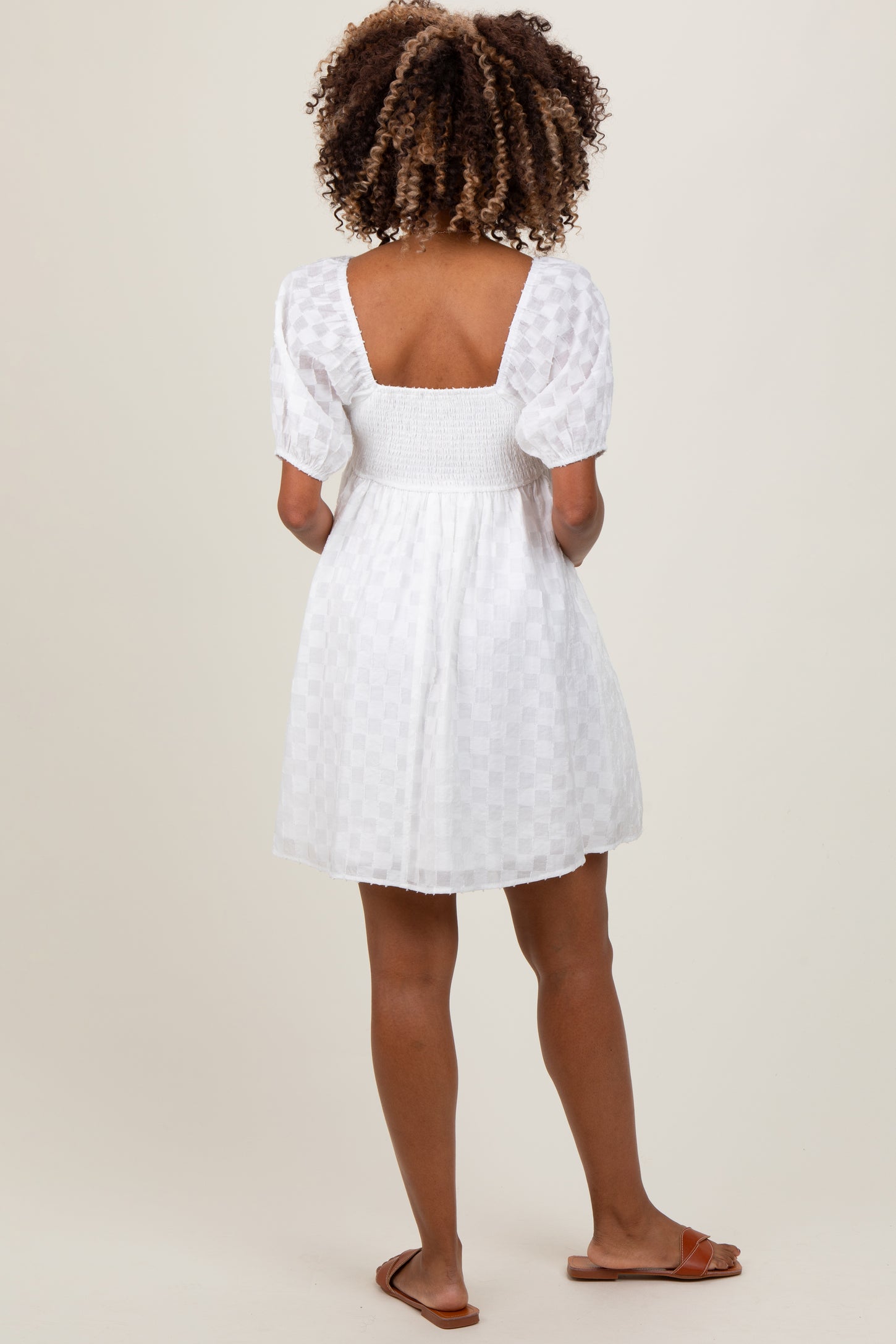 woman wearing a white maternity dress with a smocked bodice and puff sleeves, showing her back