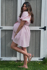 woman in a light pink short sleeve maternity dress showing her baby bump while standing next to a wooden fence