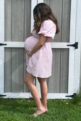 woman wearing a pink short sleeve maternity dress, showcasing her baby bump against a rustic background
