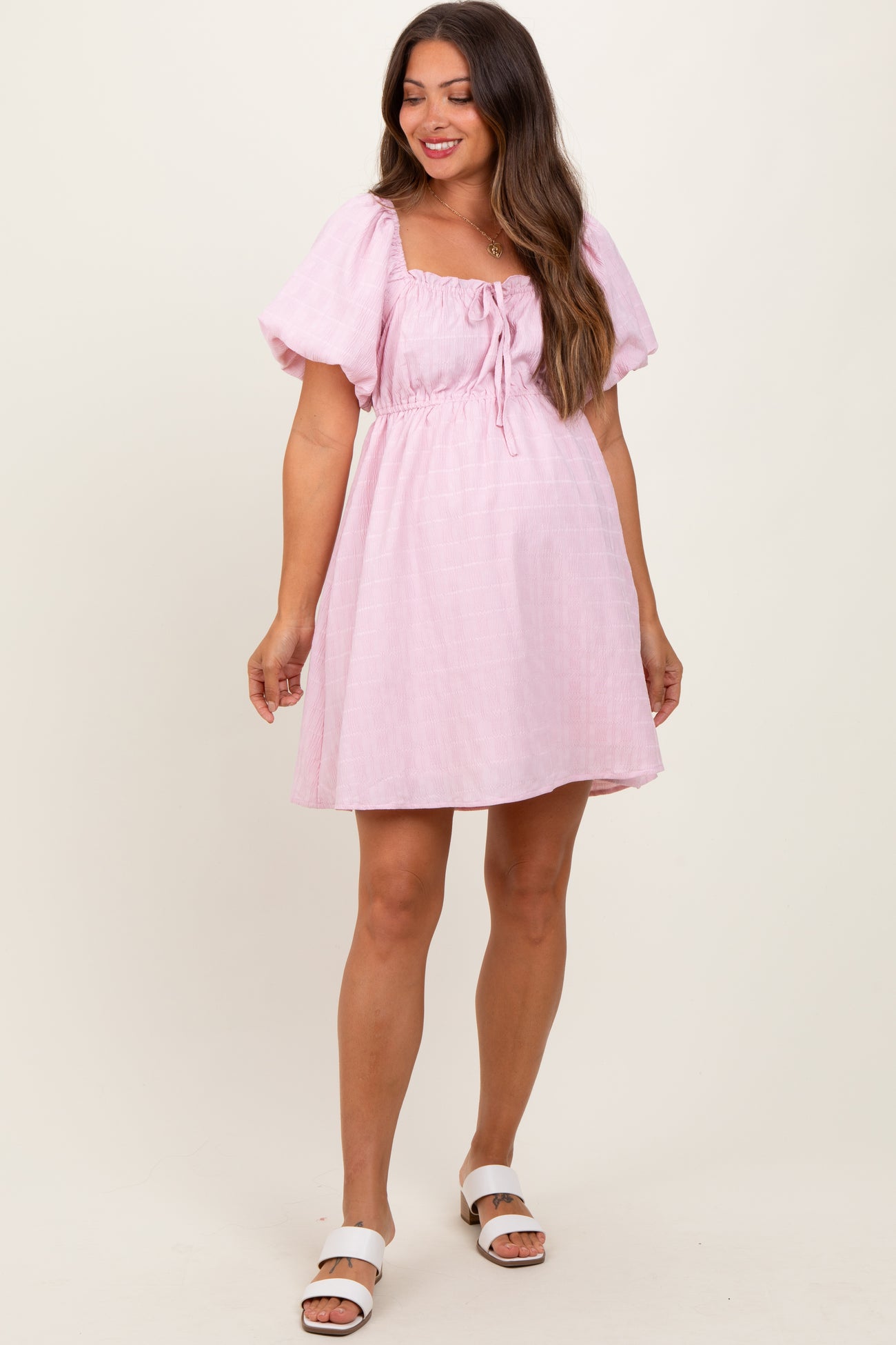 woman wearing a light pink short sleeve maternity dress with a square neckline and drawstring front detail