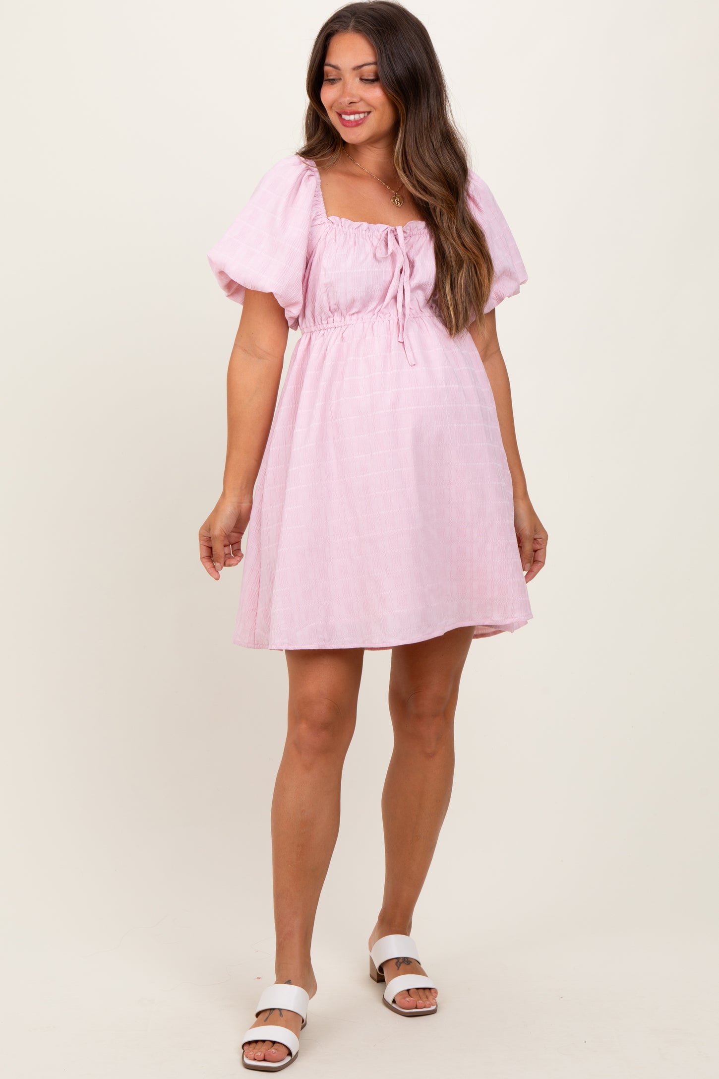 woman wearing a light pink short sleeve maternity dress with a square neckline and drawstring front detail
