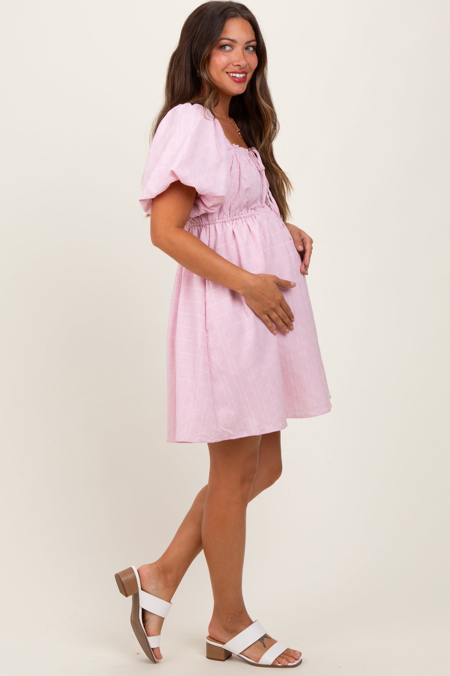 woman wearing a pink short sleeve maternity dress with a cinched waist and holding her baby bump