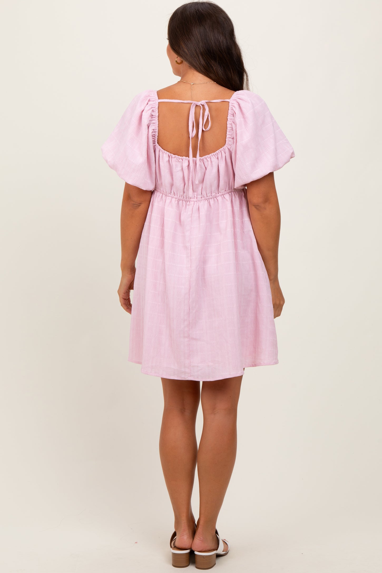 woman wearing a pink short maternity dress with puff sleeves and a back tie detail