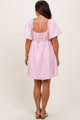 woman wearing a pink short maternity dress with puff sleeves and a back tie detail