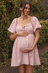woman wearing a blush pink short puff sleeve maternity dress and holding her baby bump