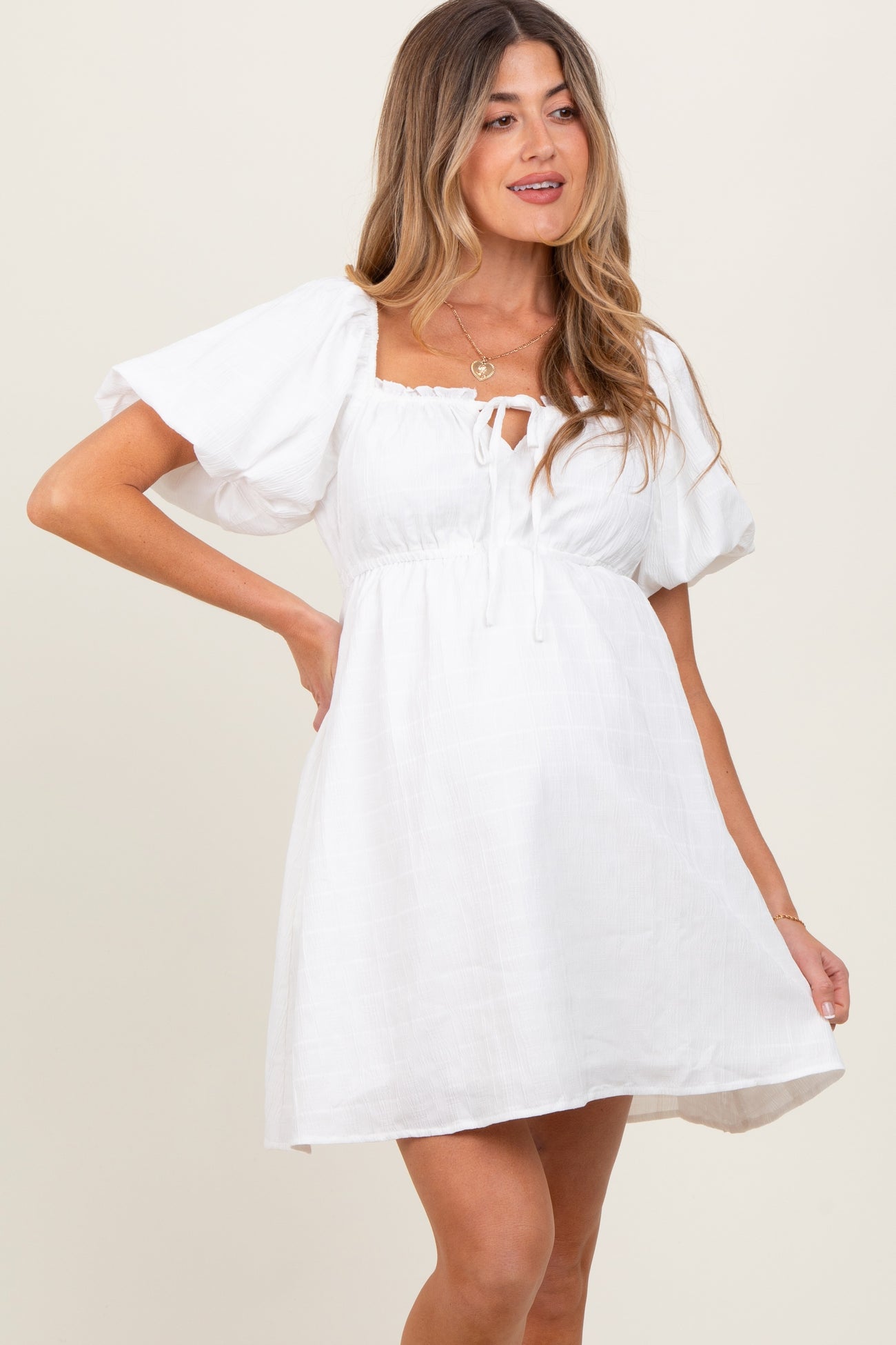 woman wearing a white short puff sleeve maternity dress with a square neckline and tie-front detail