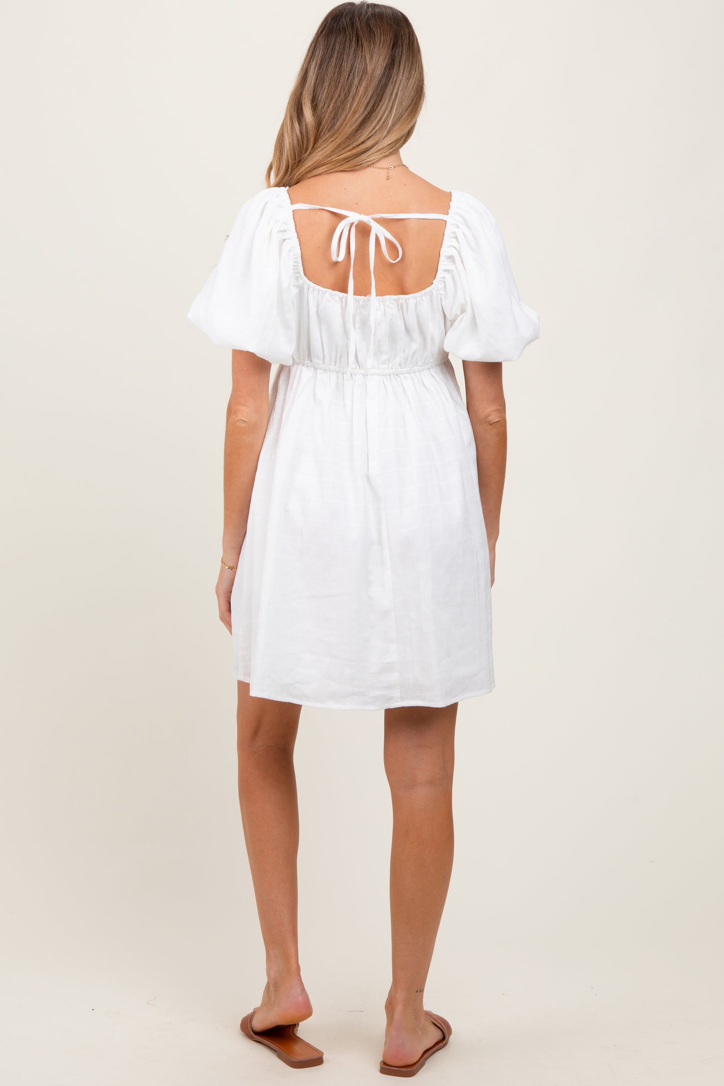woman wearing a white maternity dress with puff sleeves and a tie detail at the back, showing a baby bump