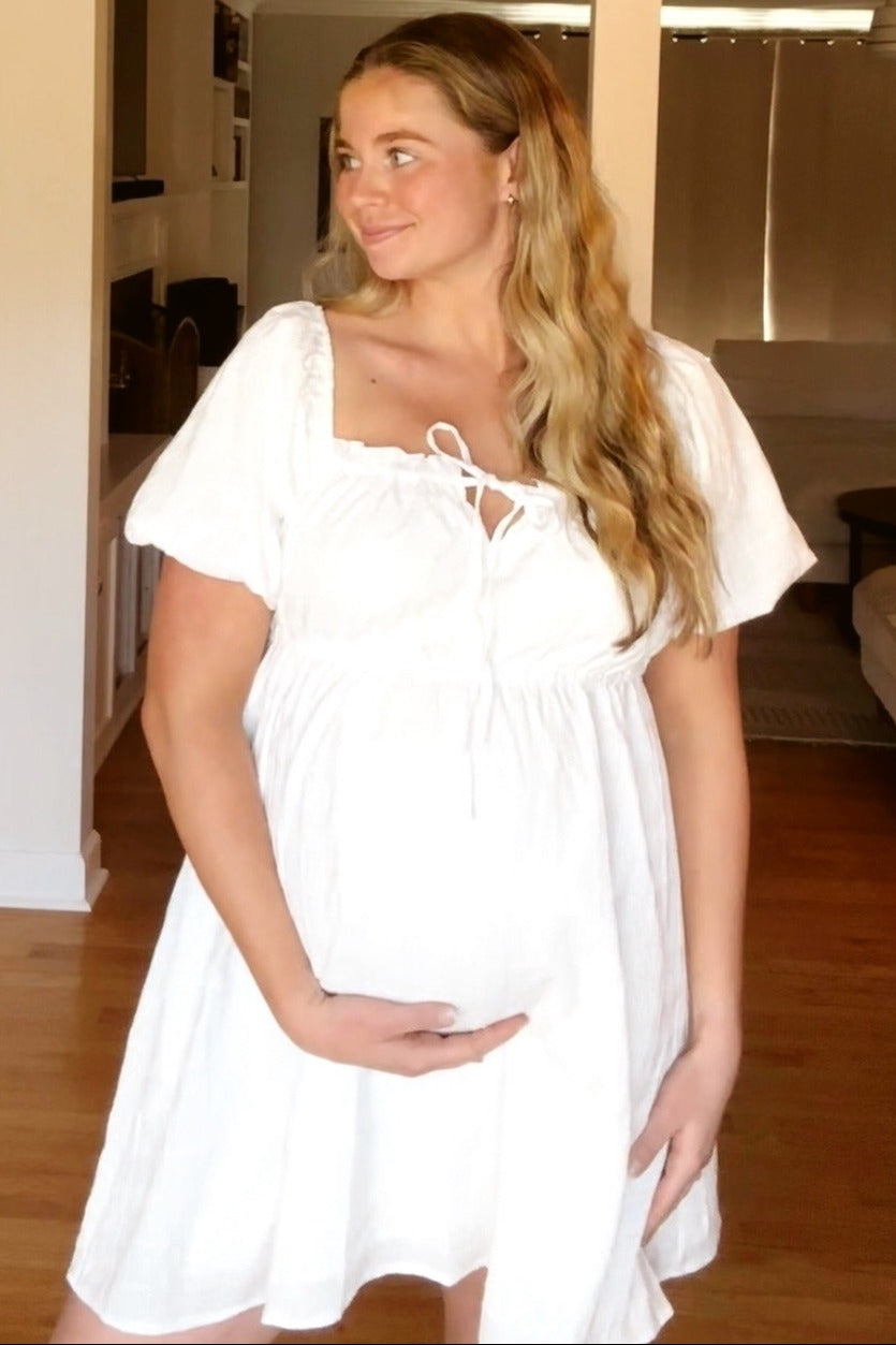 woman wearing a white short sleeve maternity dress and holding her baby bump