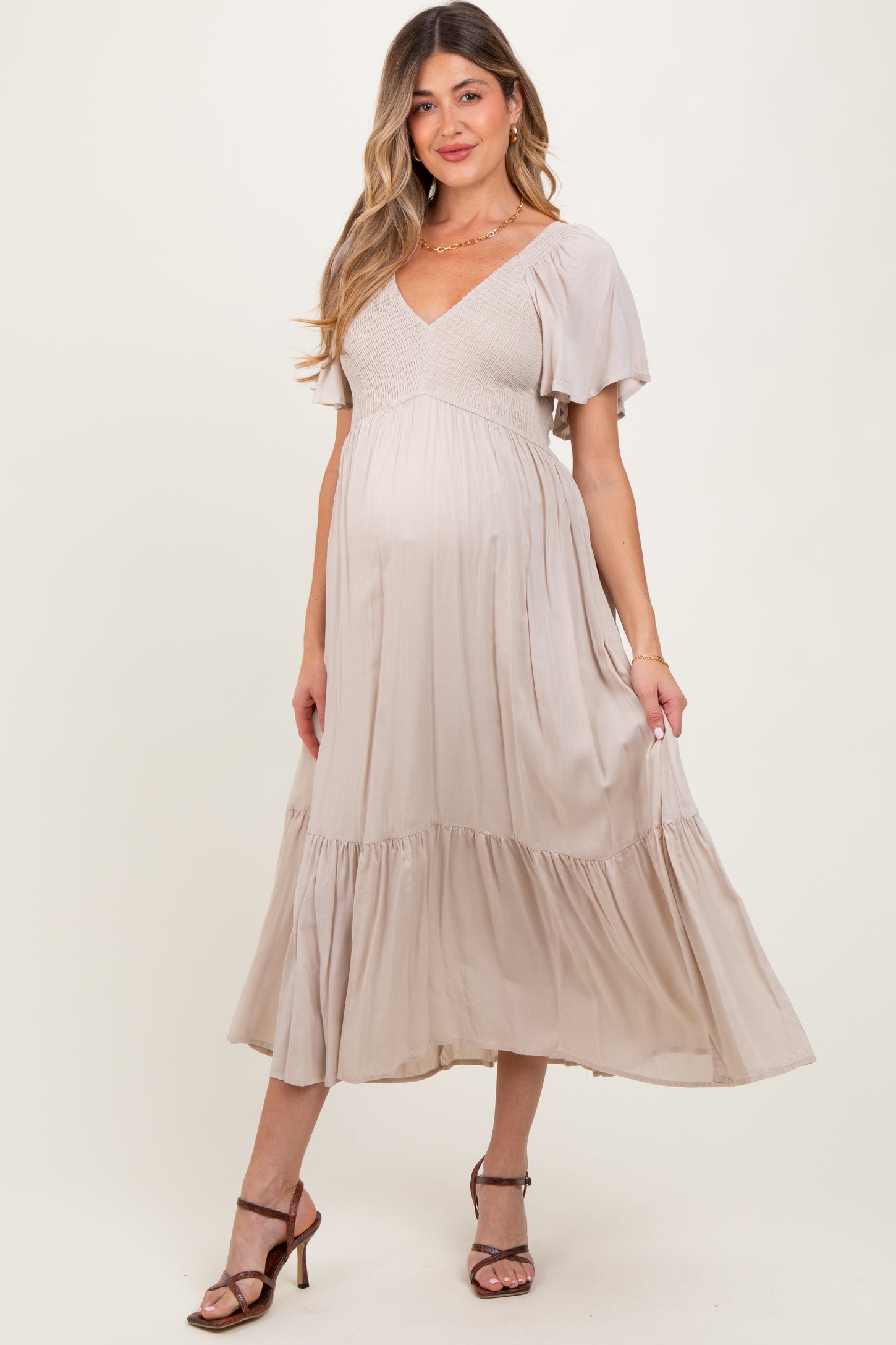 woman wearing a beige maternity dress with a puff sleeve, textured bodice, and tiered skirt, showing her baby bump