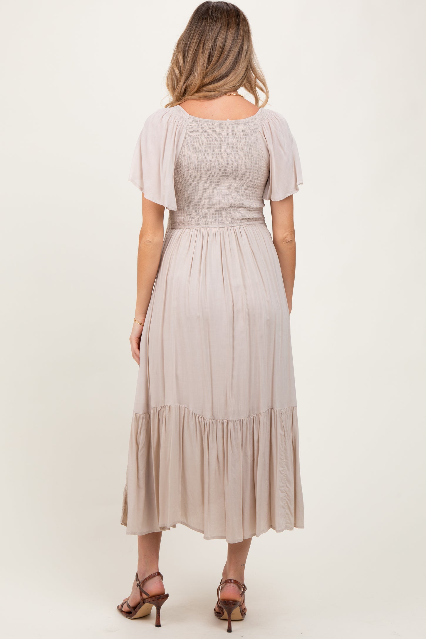 woman wearing a beige maternity dress with a smocked bodice and flutter sleeves, showcasing a flowy skirt