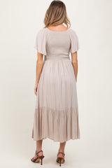 woman wearing a beige maternity dress with a smocked bodice and flutter sleeves, showcasing a flowy skirt