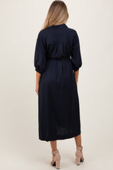 woman wearing a navy blue maternity dress with a belted waist and three-quarter length sleeves, viewed from the back