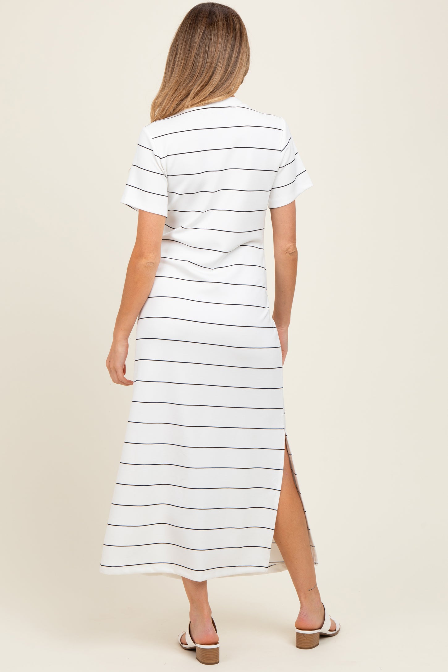 woman wearing a white maternity maxi dress with navy stripes and short sleeves, showing a side slit