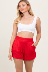 woman wearing a white cropped tank top and red elastic waist shorts with side pockets