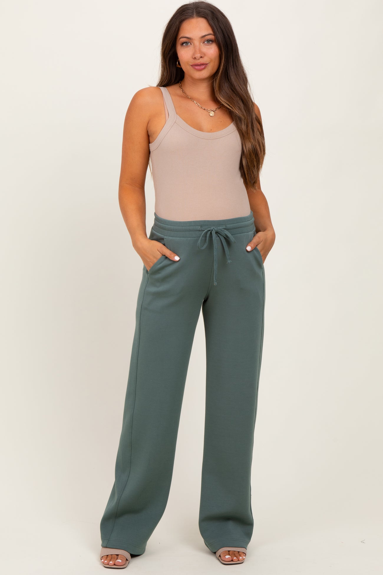 woman wearing a beige ribbed maternity bodysuit and green maternity sweatpants with pockets and a drawstring waist