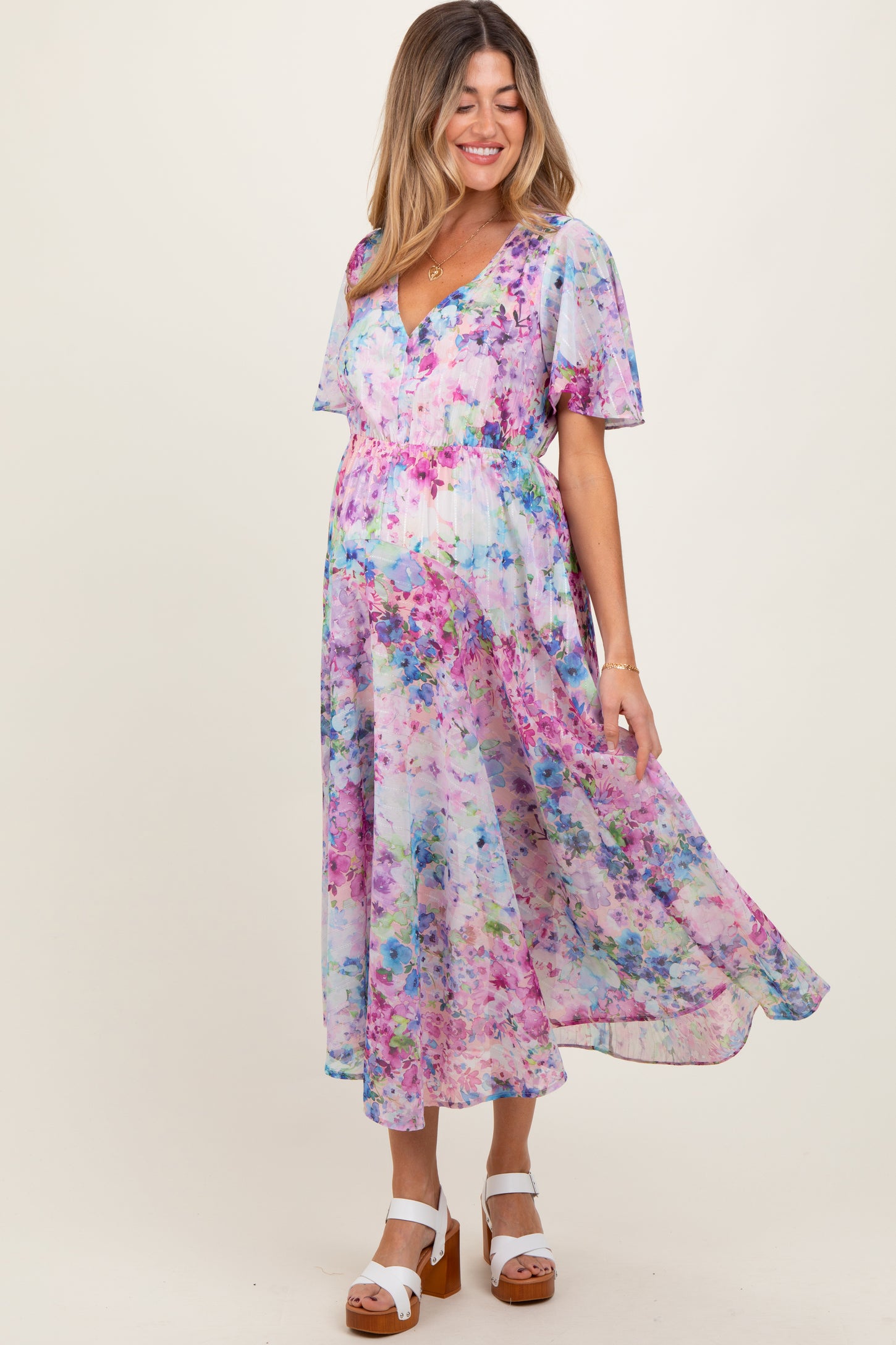 woman wearing a pastel floral print maternity dress with flutter sleeves and a flowy skirt, highlighting her baby bump