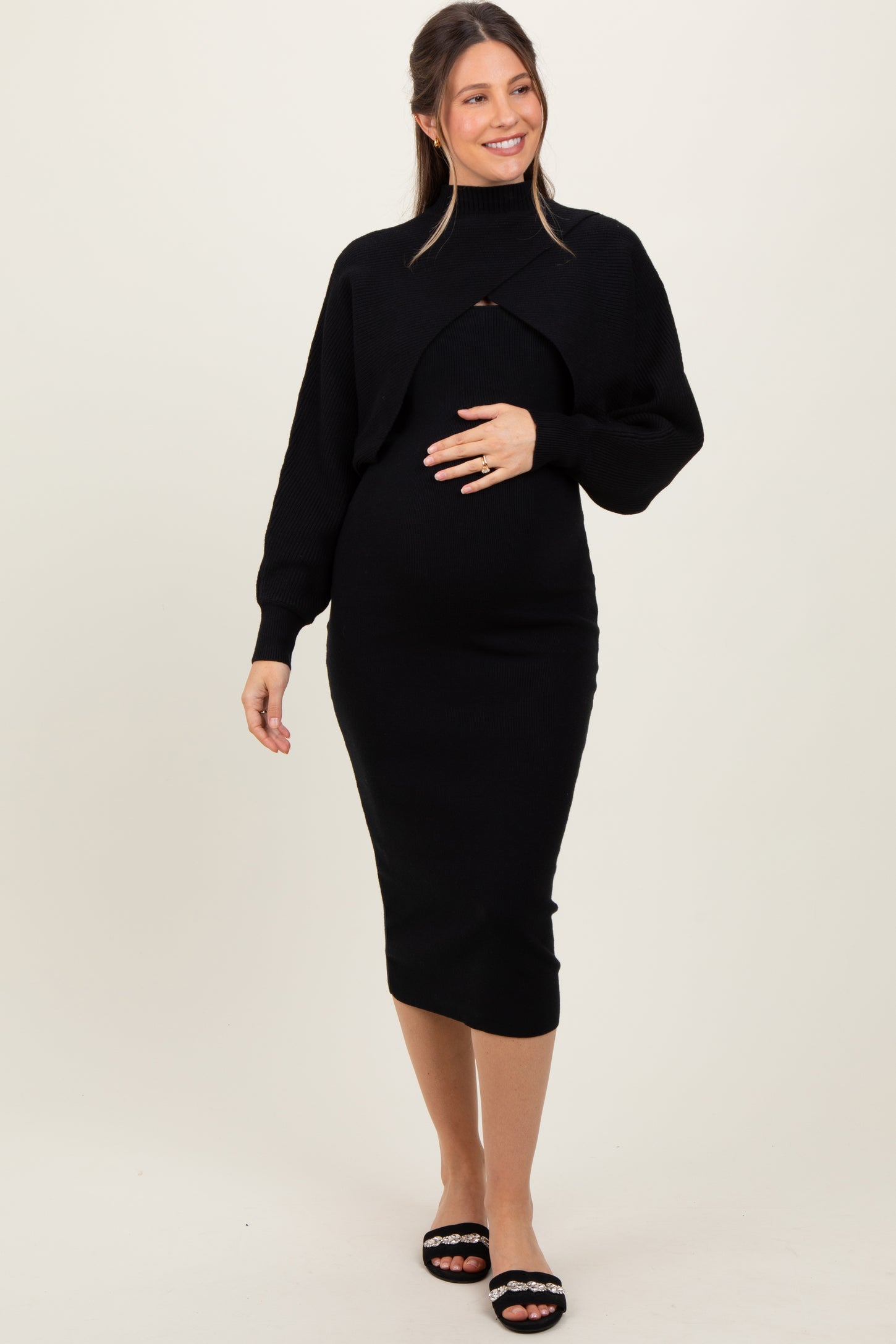 woman wearing a black maternity dress with a cropped sweater and holding her baby bump