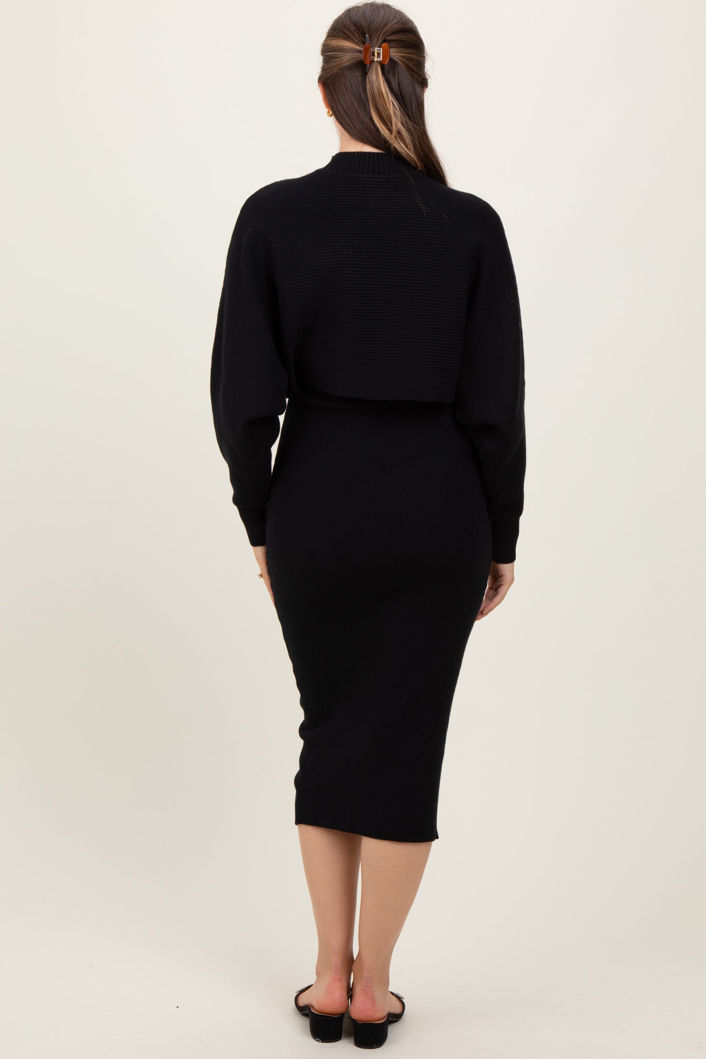 woman wearing a black knitted maternity dress with a fitted silhouette and long sleeves, viewed from the back