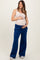 woman wearing a beige maternity tank top and blue maternity jogger pants, gently cradling her baby bump