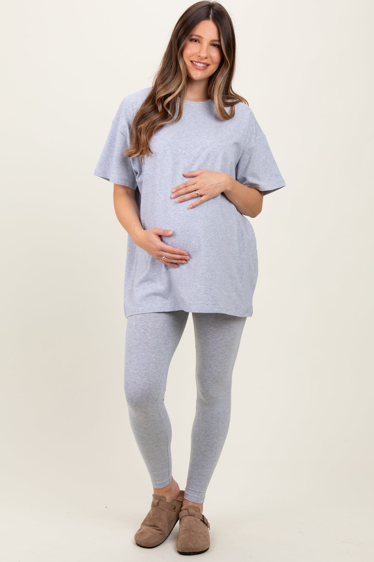 woman wearing a light gray maternity t-shirt and matching leggings, holding her baby bump