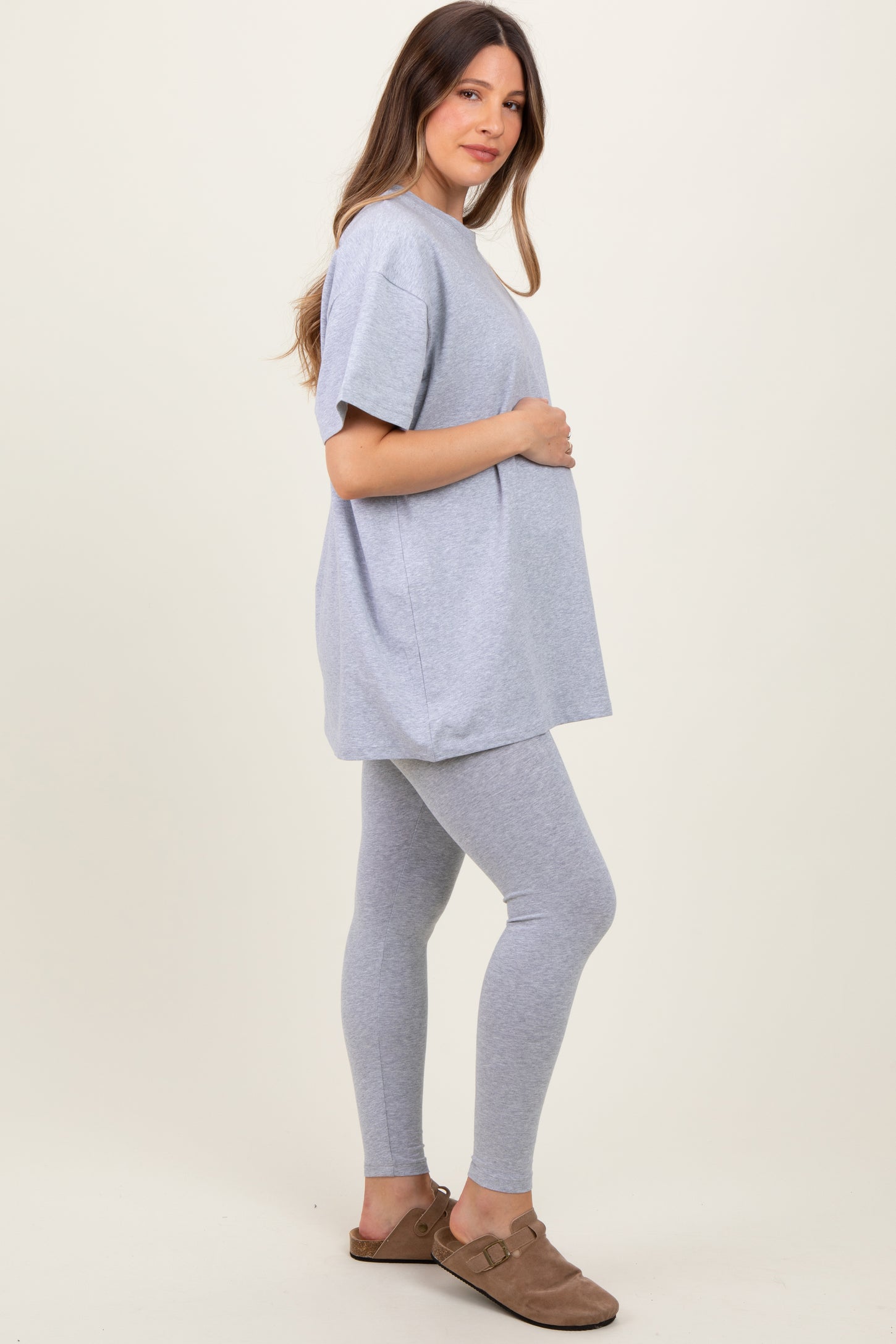woman wearing a gray oversized maternity t-shirt and gray leggings, holding her baby bump